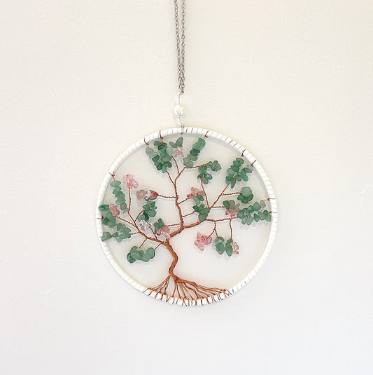 A green aventurine wire wrap wall decoration featuring a tree of life design. The decoration is approximately 20cm in diameter, with vibrant green aventurine chips intricately wrapped in copper wire, suspended in a circular metal frame. The piece is displayed against a white background, highlighting its natural beauty and detailed craftsmanship. | Simply Esoteric