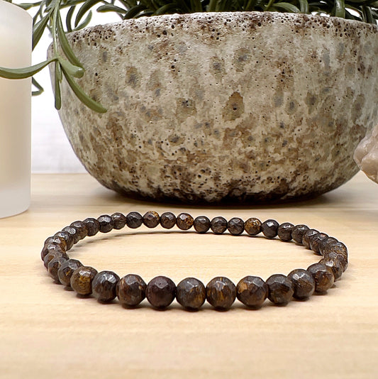 Handmade Bronzite faceted bead bracelet with 4mm round beads on stretchy cord, featuring earthy brown stones with golden-bronze shimmer, displayed on a wooden surface. | Simply Eosteric