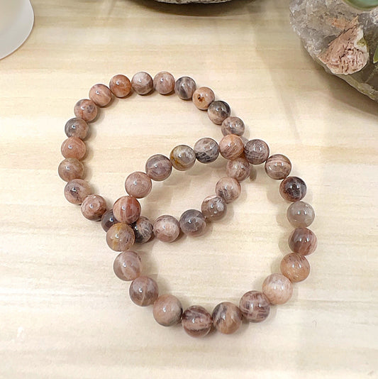 Handmade Black Moonstone crystal bead bracelets with 8mm round beads on stretchy cord, featuring smoky grey and brown tones with subtle shimmer, displayed on a wooden surface. | Simply Esoteric