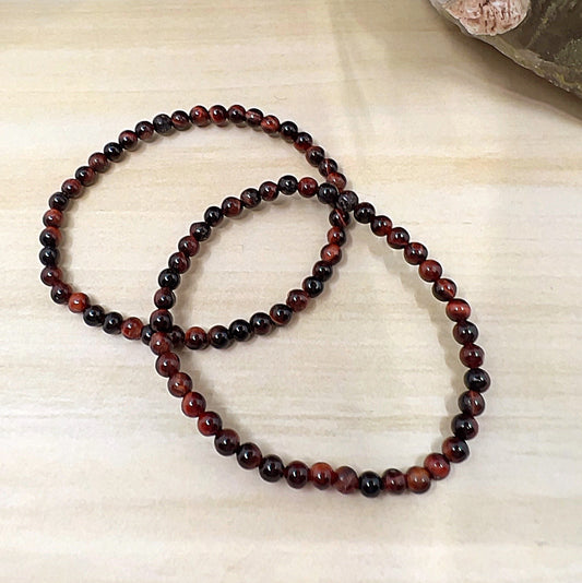 Handmade Red Tiger Eye crystal bead bracelets with 4mm round beads on stretchy cord, featuring deep reddish-brown stones with natural shimmer, displayed on a wooden surface. | Simply Esoteric