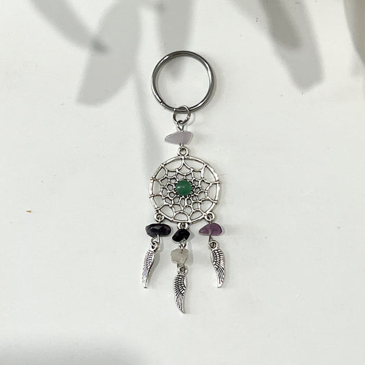 A dream catcher keyring featuring a circular design with a green aventurine stone in the center, adorned with purple and green crystal chips. Three silver feather charms hang from the bottom, enhancing the keyring's intricate and decorative appearance. | Simply Esoteric