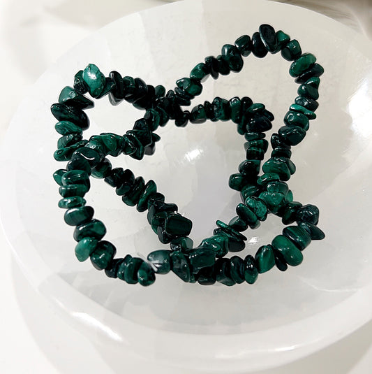 A set of malachite chip bracelets displayed on a white surface. The bracelets feature rich, deep green malachite chips with intricate banding patterns, strung together to form a stretchy and flexible accessory. | Simply Esoteric
