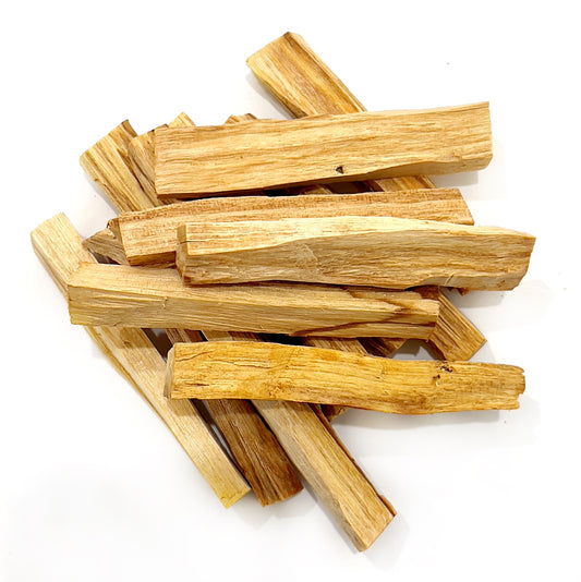 A pile of Palo Santo wood sticks, with a natural golden-brown color, arranged haphazardly on a white background. Each stick shows the distinctive grain and texture of the sacred wood, traditionally used for smudging and purification practices. | Simply Esoteric