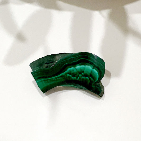 A polished malachite slice measuring 43mm x 22mm x 7mm, featuring intricate banding patterns in deep and vibrant green hues. | Simply Esoteric