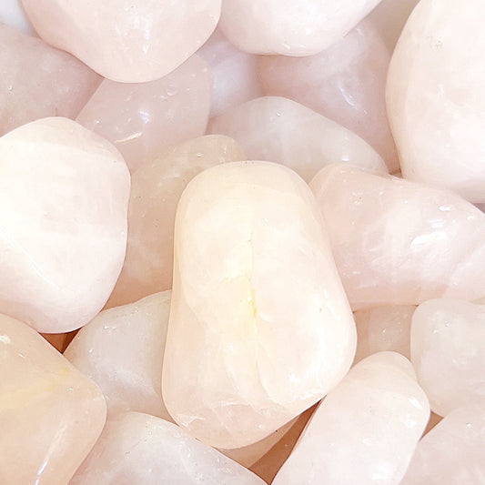 An assortment of rose quartz tumbled stones, bathed in soft light, revealing their translucent pale pink hues. Each stone is smooth with rounded edges, offering a sense of calm and nurturing love, arranged in a cluster that emphasizes their collective beauty and individual uniqueness. | Simply Esoteric