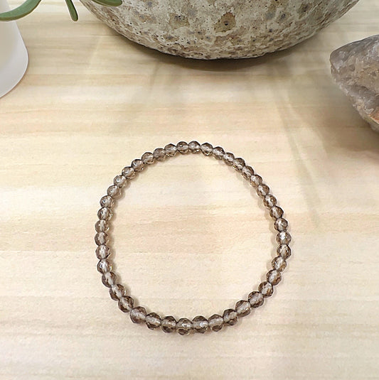 Handmade Smoky Quartz faceted crystal bead bracelet with 4mm translucent brown beads on stretchy cord, displayed on a light wooden surface with natural stone decor. | Simply Esoteric
