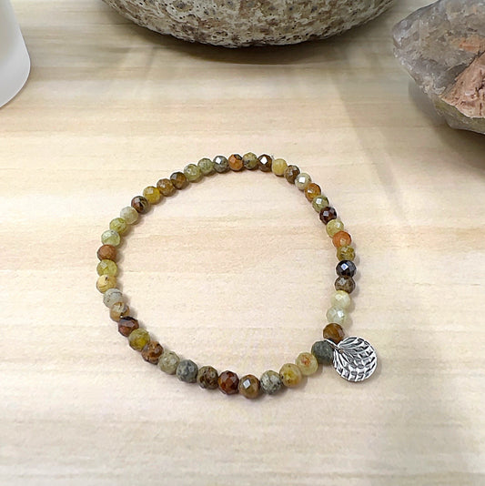 Handmade Green Garnet faceted crystal bead bracelet with 4mm round beads on stretchy cord, featuring earthy green, gold, and brown tones with a silver charm, displayed on a wooden surface. | Simply Esoteric