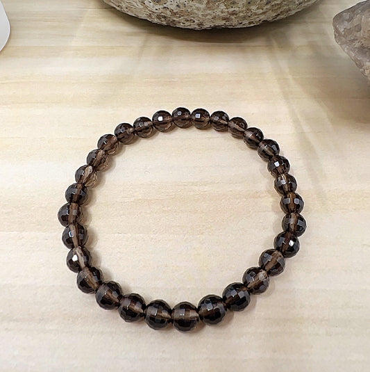 Handmade Smoky Quartz faceted crystal bead bracelet with 6mm round beads on stretchy cord, featuring dark smoky brown stones that reflect light, displayed on a wooden surface. | Simply Esoteric