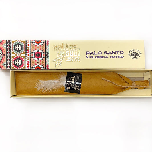 An open box of 'Native Soul Incense Smudge Sticks' featuring 'Palo Santo & Florida Water' lies against a white background. The left side of the box is decorated with colorful, traditional tribal patterns, while the right side has elegant, golden text on a cream backdrop. Inside, the smudge stick is neatly wrapped in brown paper, tied with twine and adorned with a soft white feather, conveying a sense of natural purity and ritualistic tradition. | Simply Esoteric