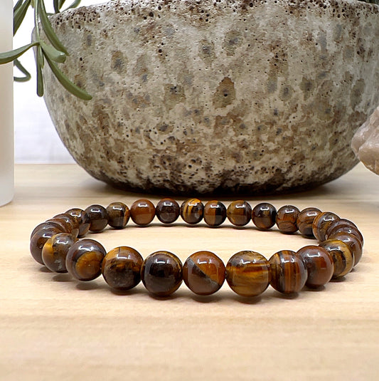 Handmade Tiger Eye crystal bead bracelet with 6mm round beads on stretchy cord, featuring golden-brown stones with natural shimmer, displayed on a wooden surface. | Simply Esoteric