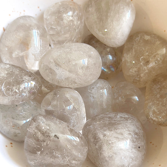 A collection of smokey quartz tumbled stones clustered together, their translucent, misty surfaces ranging from light to dark shades of gray and brown. The stones shimmer with a subtle brilliance, revealing faint natural inclusions and a smooth, polished texture that conveys a sense of calm strength. | Simply Esoteric