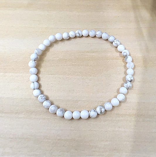 Handmade White Howlite crystal bead bracelet with 4mm round beads on stretchy cord, featuring smooth white stones with natural grey veining, displayed on a wooden surface. | Simply Esoteric
